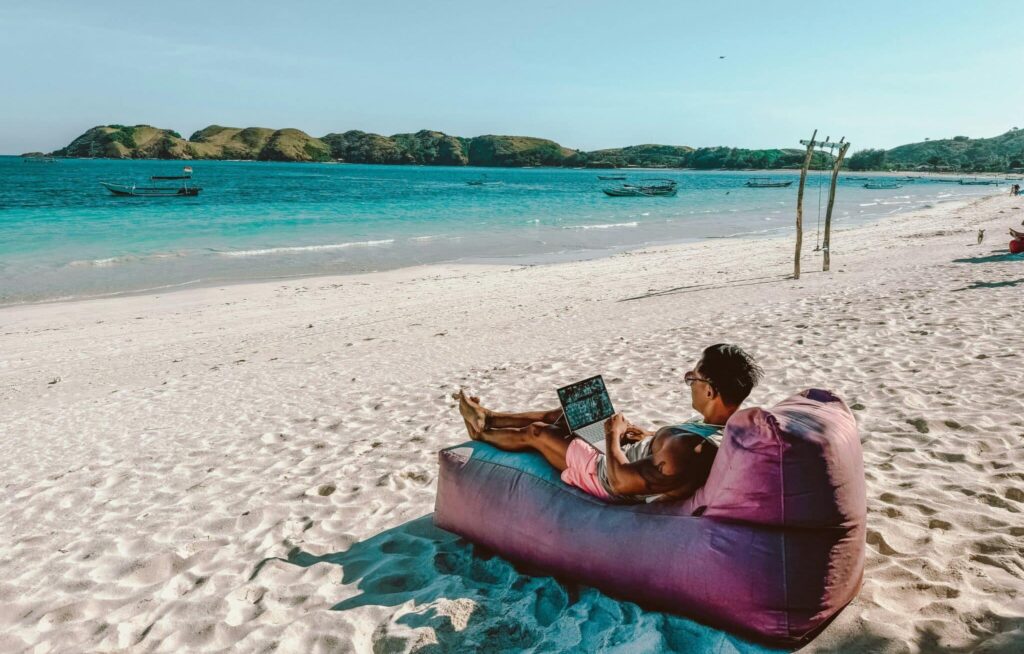 Ein mann sitzt am Strand und arbeitet am Laptop
