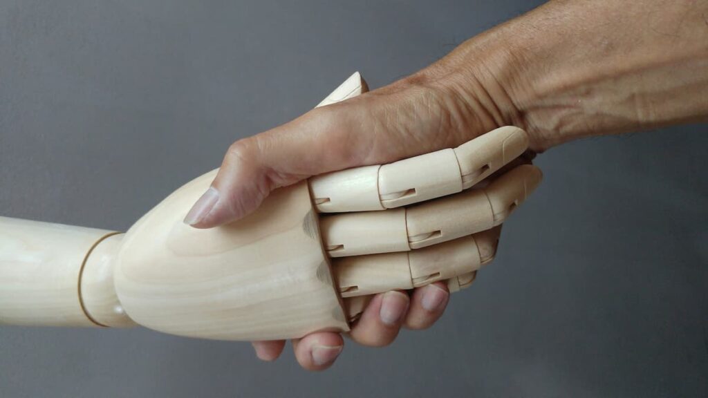 Eine mechanische Hand aus Holz und eine menschliche Hand beim Handschlag.