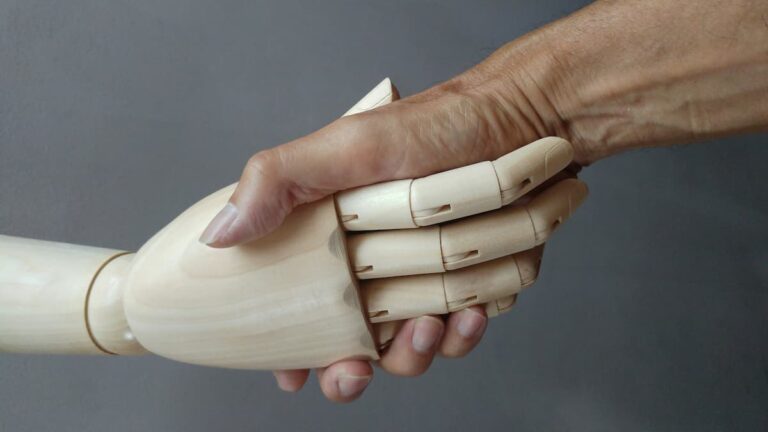 Eine mechanische Hand aus Holz und eine menschliche Hand beim Handschlag.